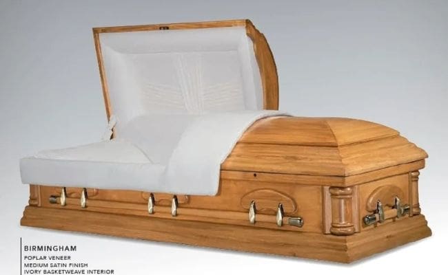A wooden coffin with metal handles and a white cloth inside.