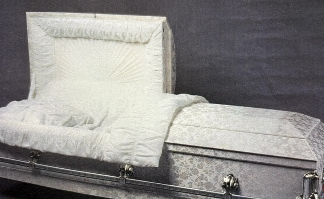 An elegant white casket with intricate fabric detailing and silver handles.
