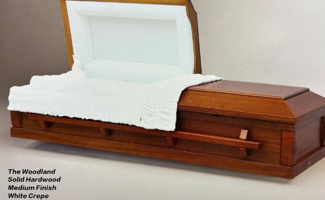 A wooden coffin with a white interior lining and a cloth draped inside.